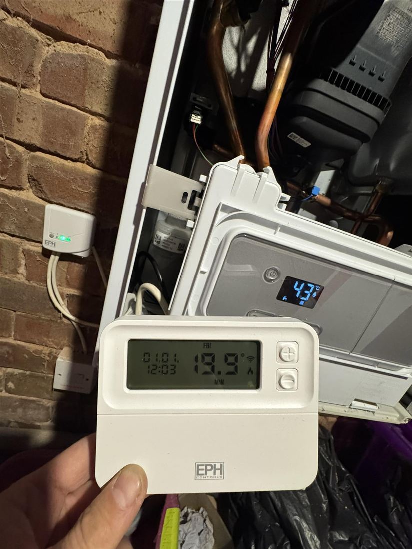 Replacement wireless thermostat held in front of a boiler